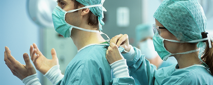 Två personer inom vården hjälper varandra att sätta på sig operationskläder