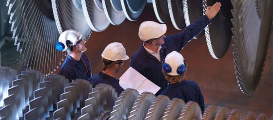 Maskinsäkerhet Människor i skyddshjälmar tittar på stora kugghjul