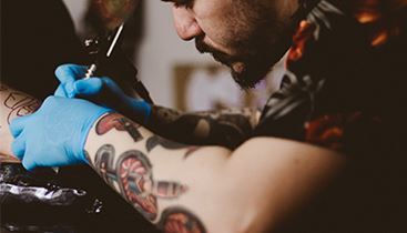 En man, med handskar och tatueringsmaskin, tatuerar en kvinnas nacke